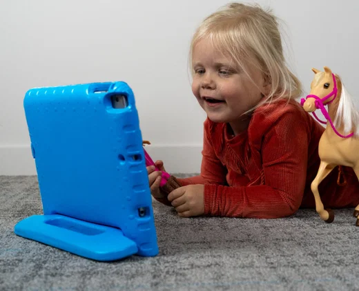 Kind kijkt naar een tablet die rechtop staat in een blauwe kinderhoes
